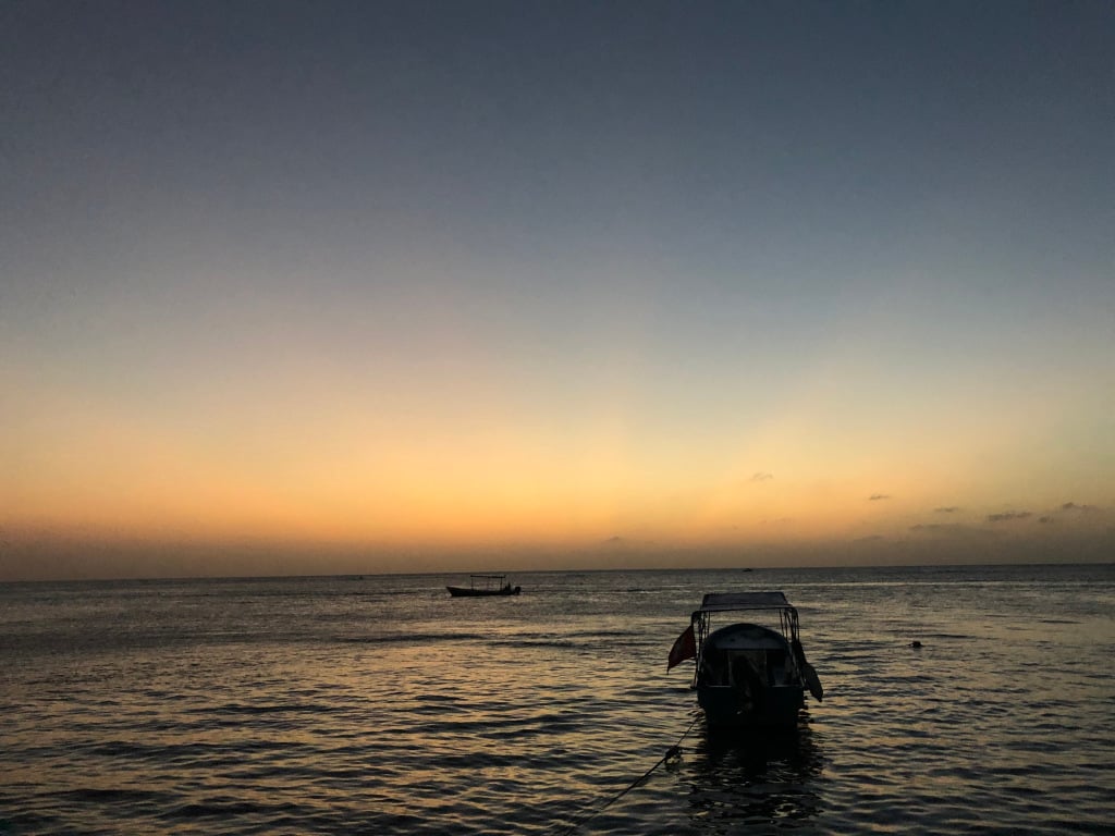 yellow and blue sunset over the Caribbean with a boat on the water and a boat in the foreground.